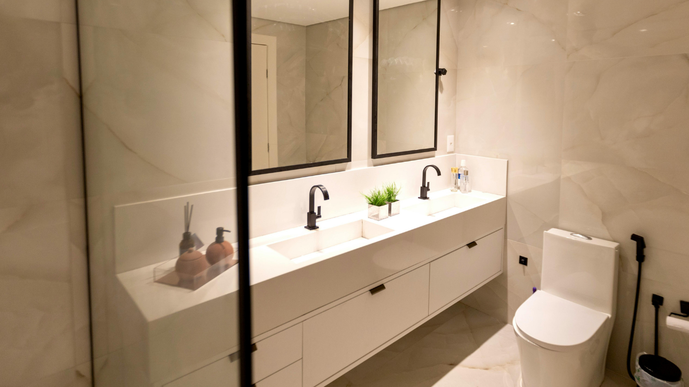Modern bathroom with white marble-like tiles, a white double vanity with black fixtures, and a white toilet.