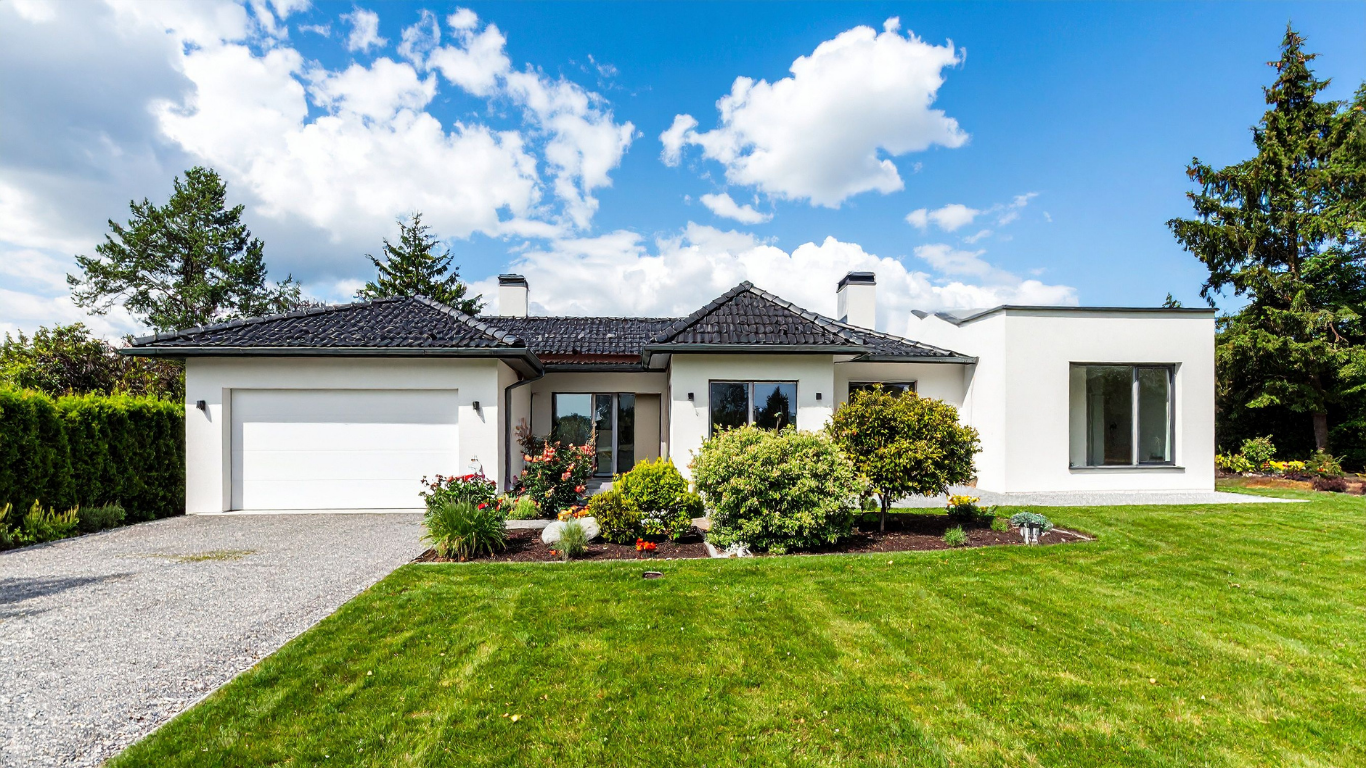 White modern house with green lawn, gravel driveway, and cloudy blue sky.