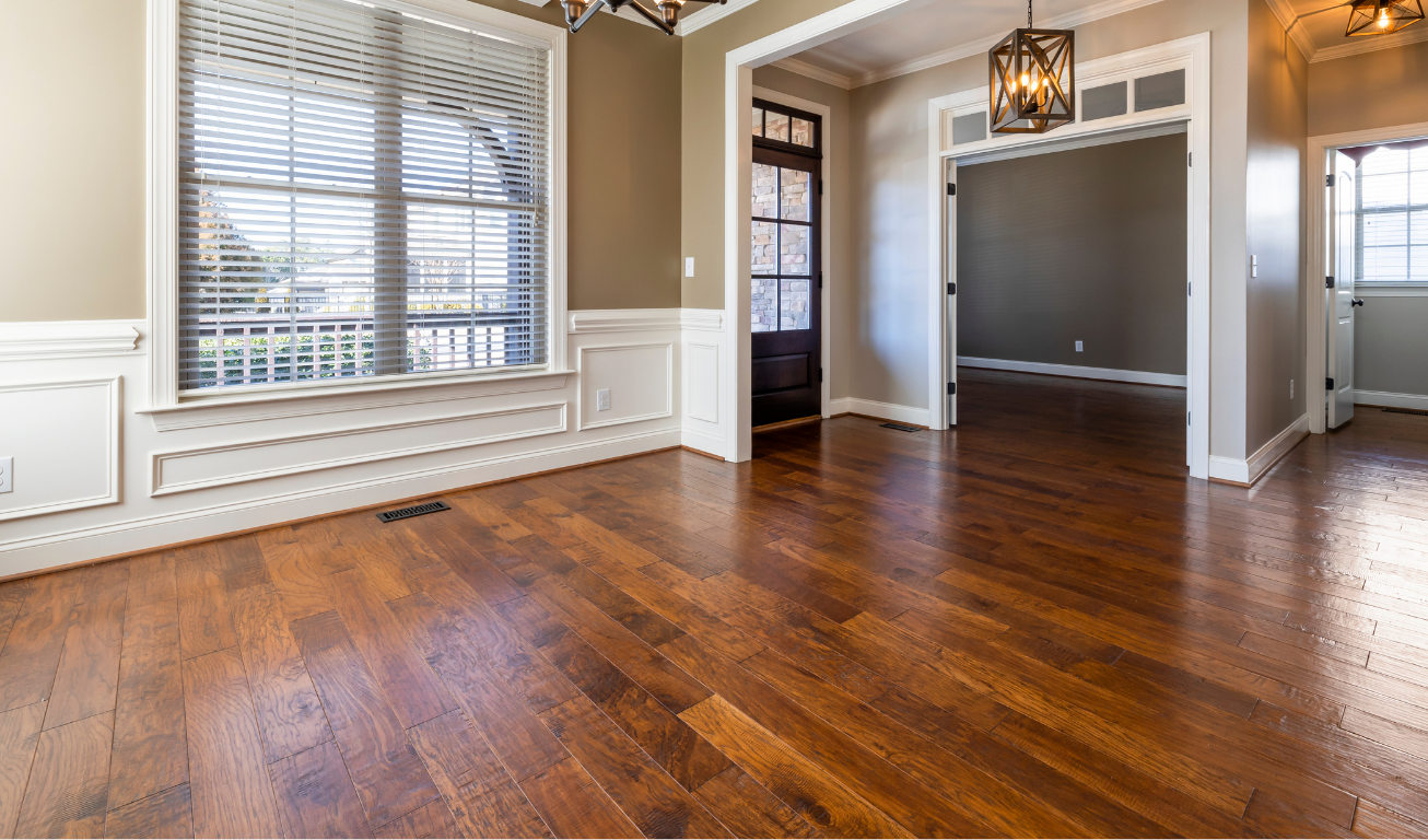 Empty dining room with hardwood floors, tan walls, white trim, and a large window.