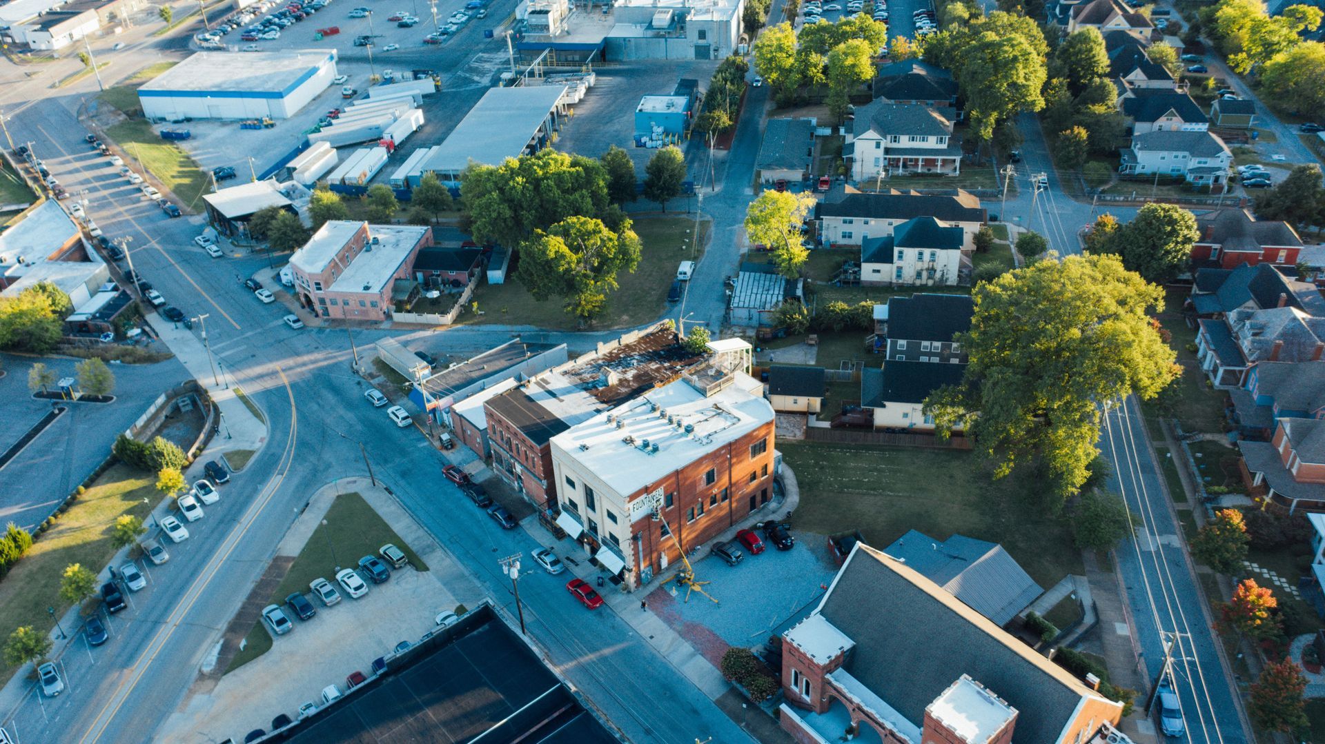 Aerial view of a downtown street with buildings, trees, parked cars, and a central brick corner building