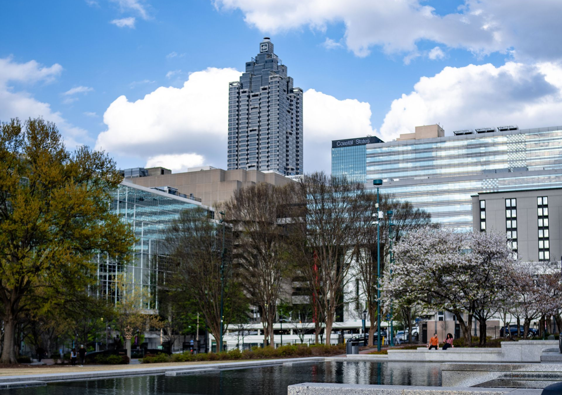 City skyline with modern buildings and a reflective waterway under a partly cloudy sky