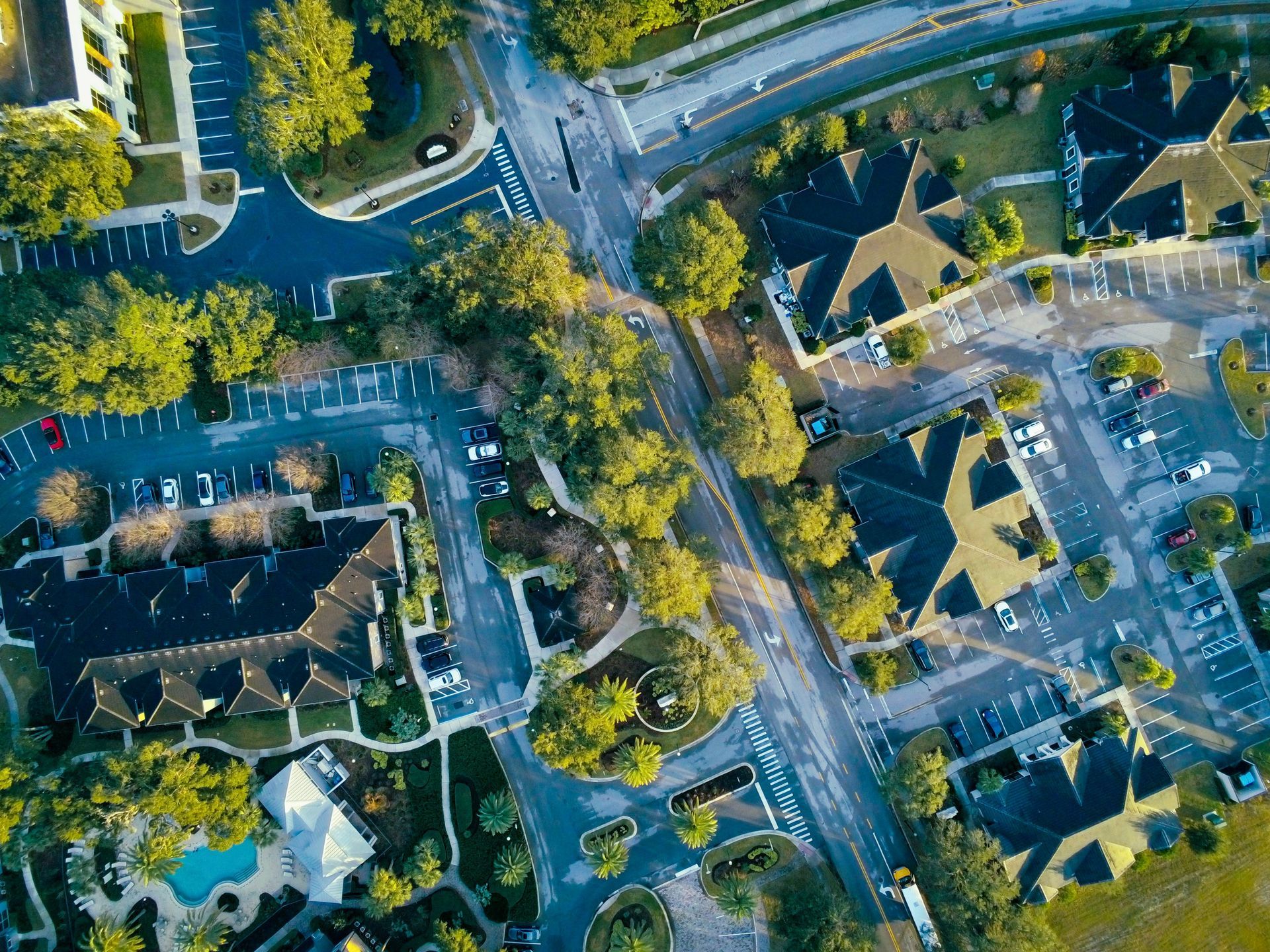 Aerial view of a suburban neighborhood with houses, tree-lined streets, and parked cars.