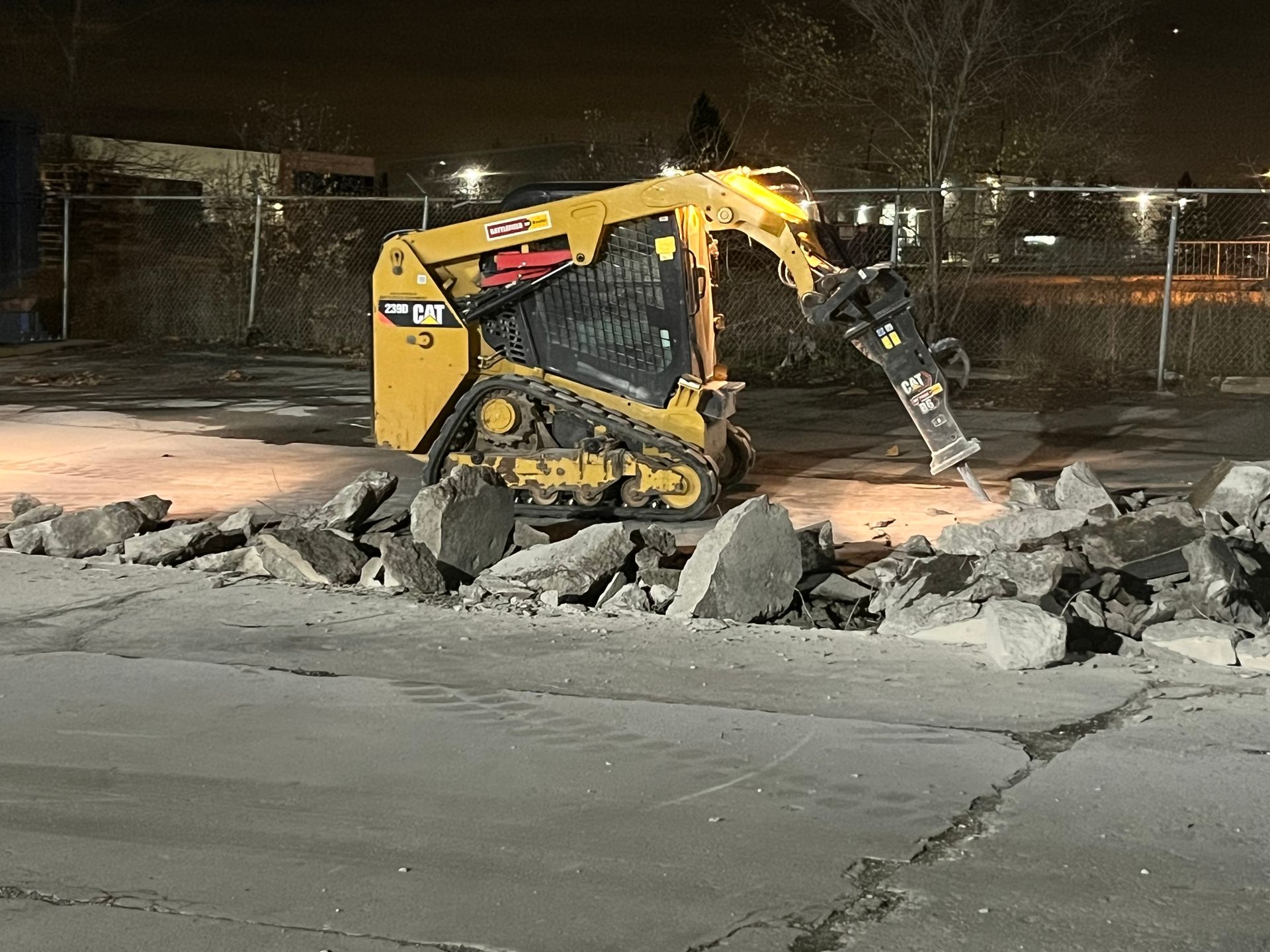 A bulldozer is breaking up concrete in a parking lot at night.