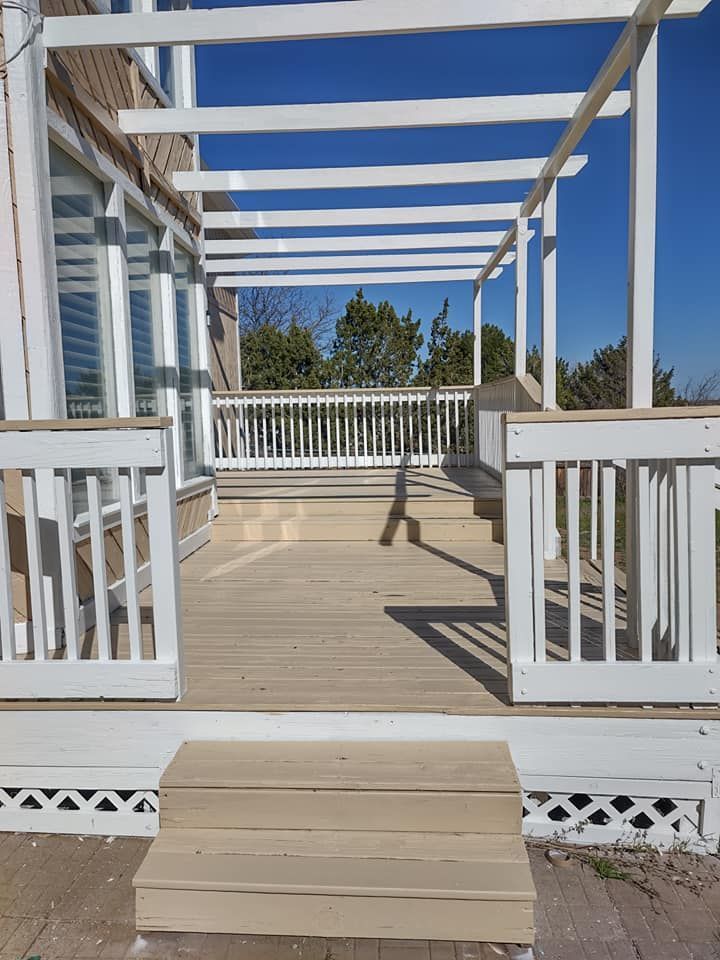 A wooden deck with new white paint pergola and stairs leading to it.