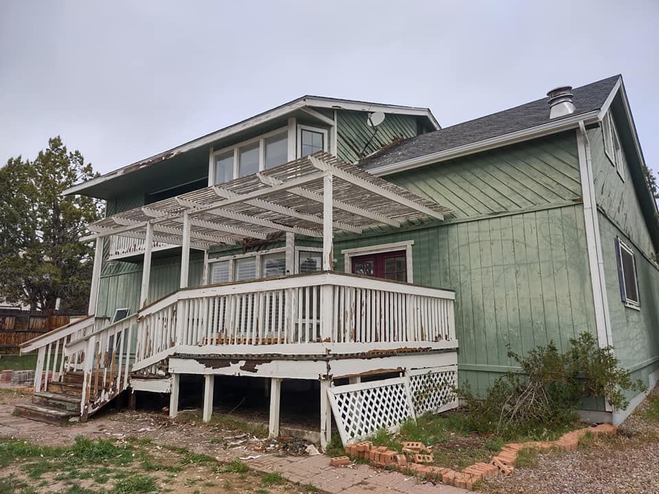 A green house with old paint and a white deck and stairs.