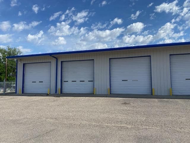 A row of white garage doors on a building with a blue roof. The building has received commercial exterior paint services