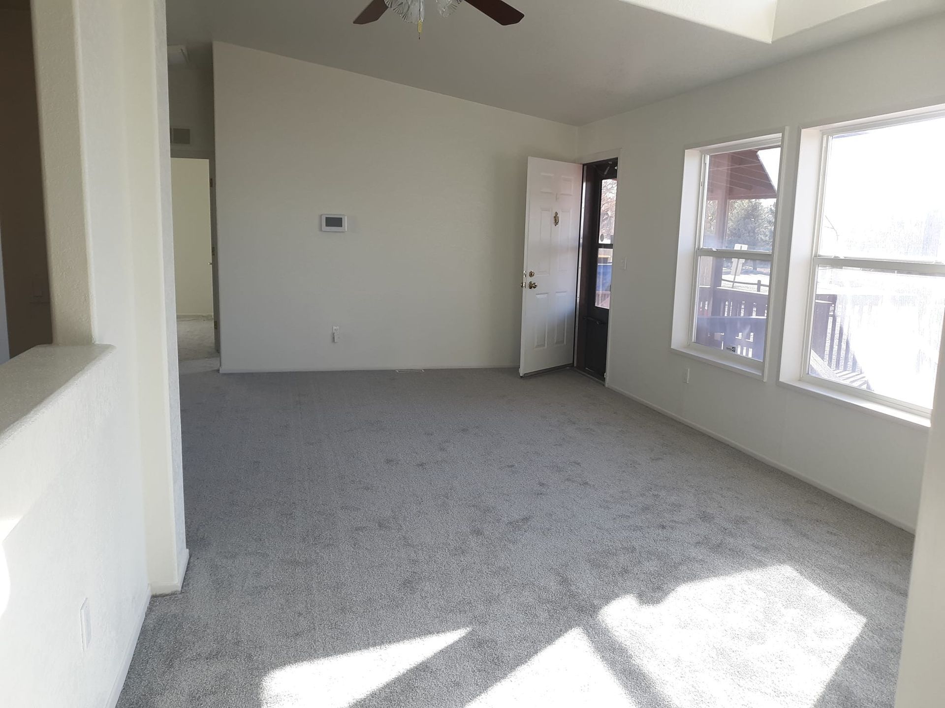 An empty living room with a ceiling fan and a lot of windows. The room has received interior painting services