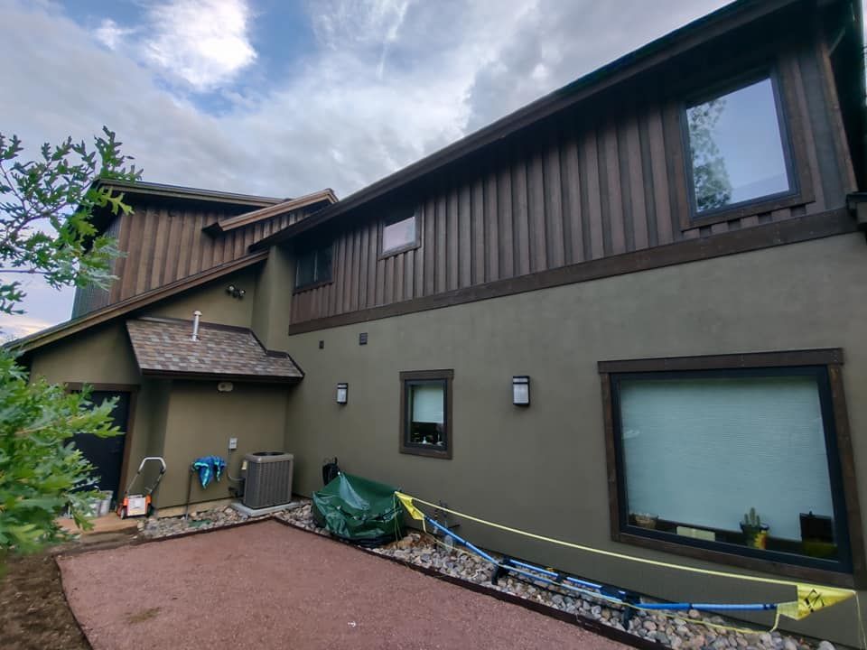 A large house with many windows and a green tarp, freshly painted with exterior services.