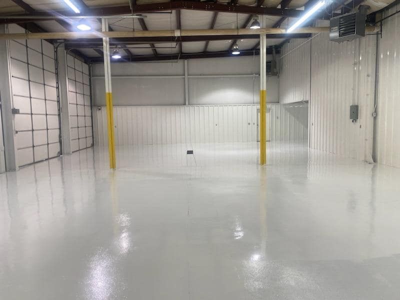 A large empty warehouse with a white floor and yellow poles. the warehouse has received floor painting services