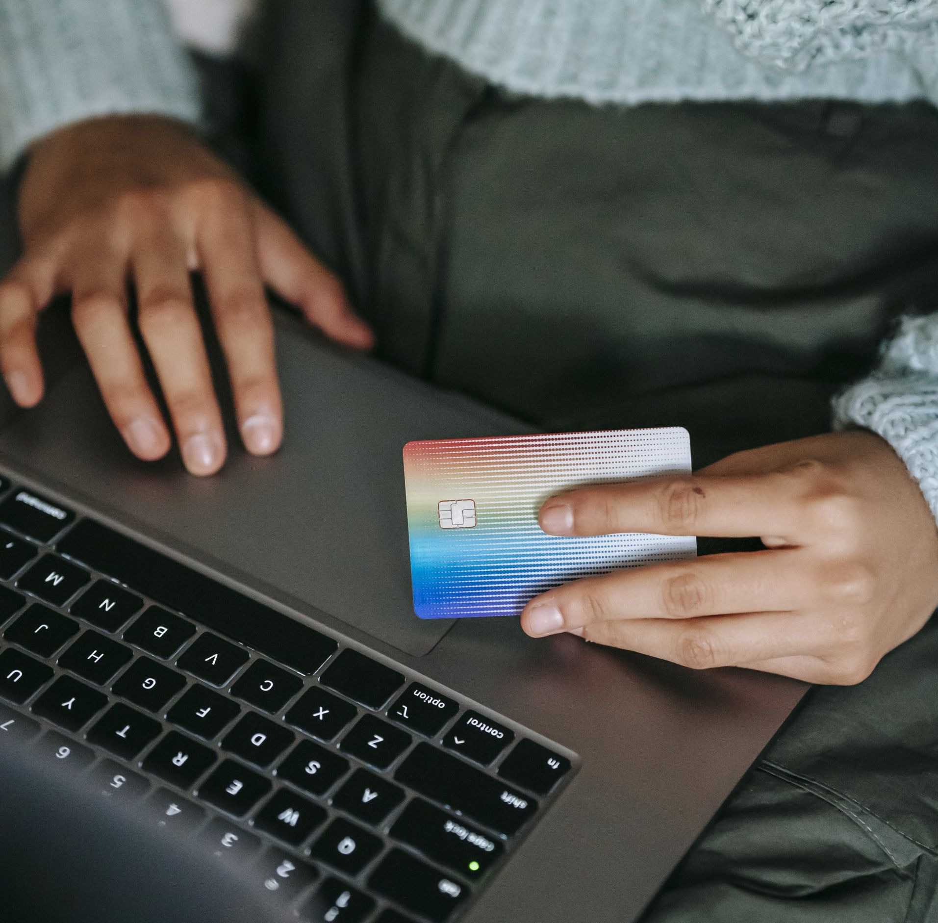Person holding a colorful credit card over a laptop keyboard, making online purchase.
