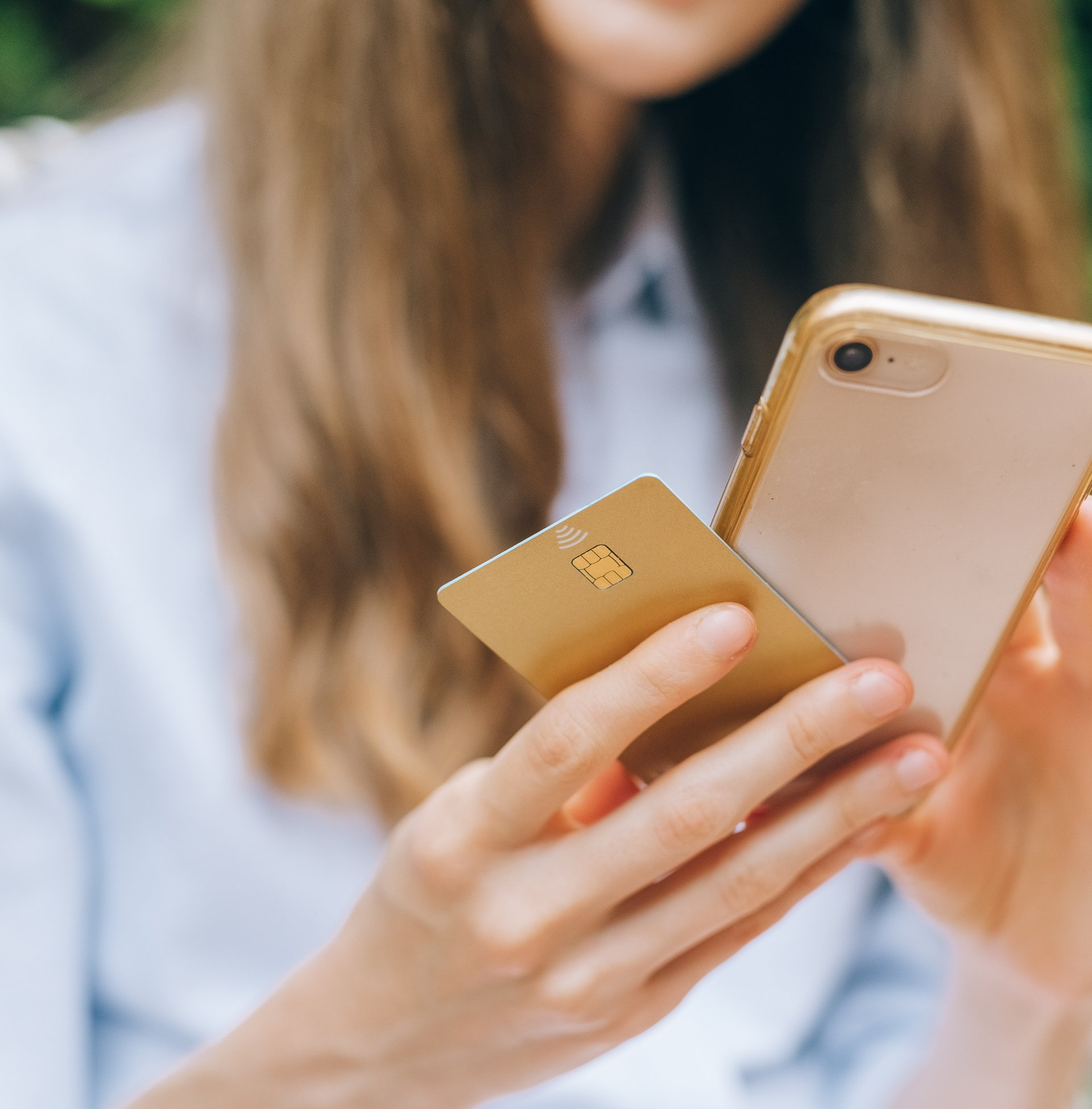 Woman holding gold phone and credit card, using them with a light blue shirt backdrop.