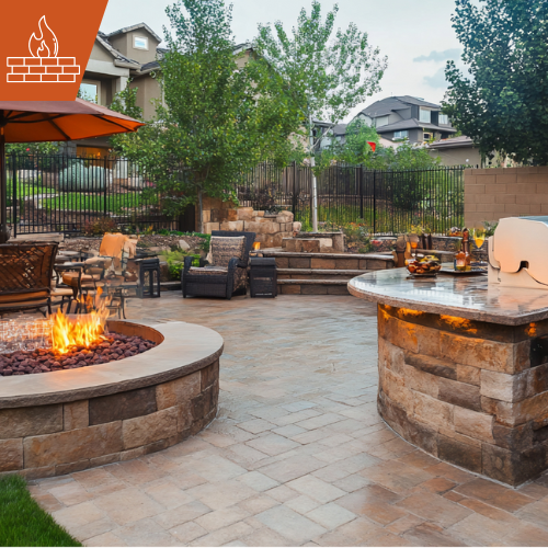 Outdoor patio with fire pit, seating, bar, and lush landscaping in the background.