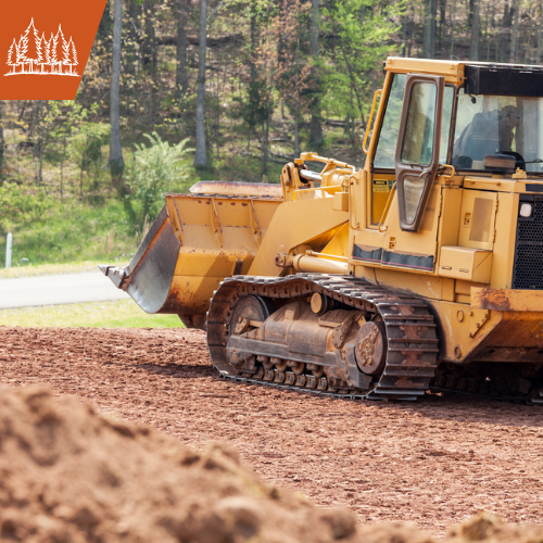 Yellow bulldozer on dirt ground, clearing land. Forest in the background.