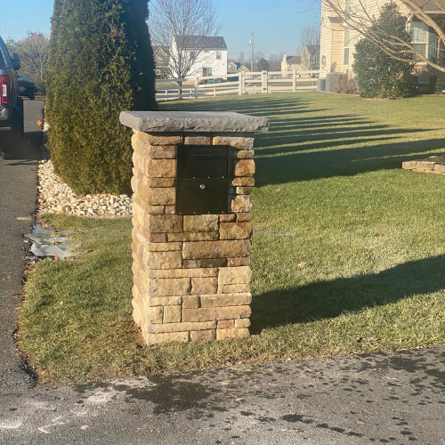 Stone mailbox with black door, cap, on a green lawn.