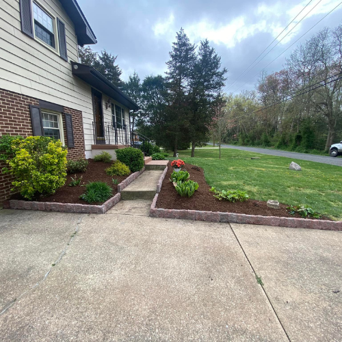 A house with a concrete driveway and landscaped garden beds filled with mulch, flowers, and bushes.