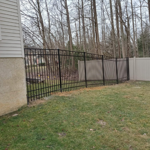 Black metal fence bordering a grassy yard near a beige house and trees.