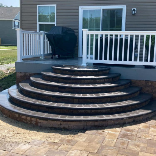 Curved brick steps leading up to a patio with white railing, adjacent to a house.