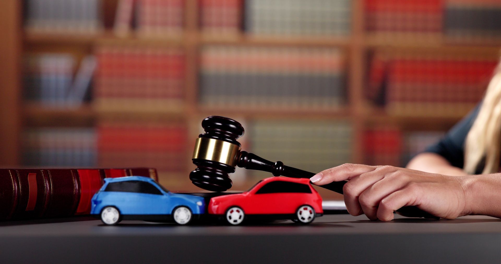 Car accident lawyer with gavel and 2 model cars over the desk.