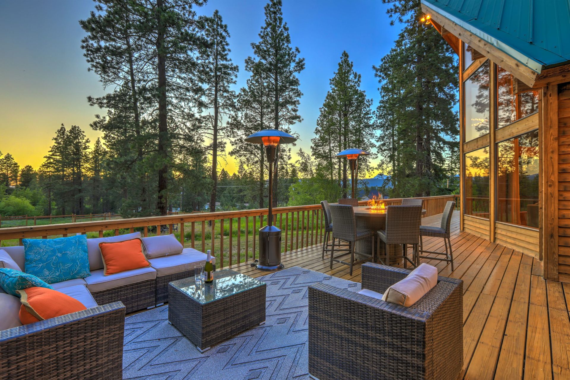 A large wooden deck with a couch , chairs , table and heaters.