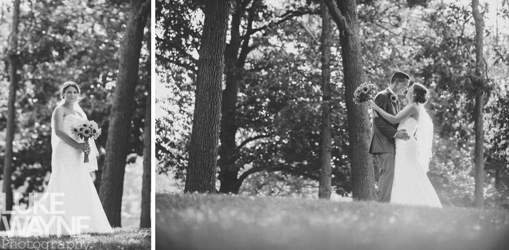 Bride and groom kissing amidst trees, holding bouquets. Black and white photo.