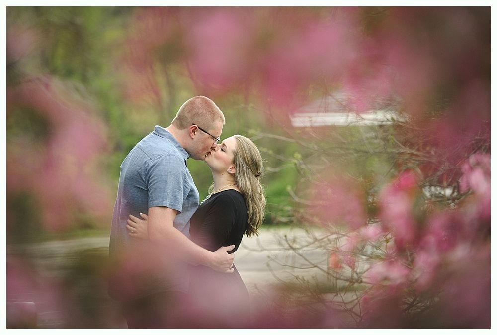 Couple kissing amidst pink blossoms in a garden setting.