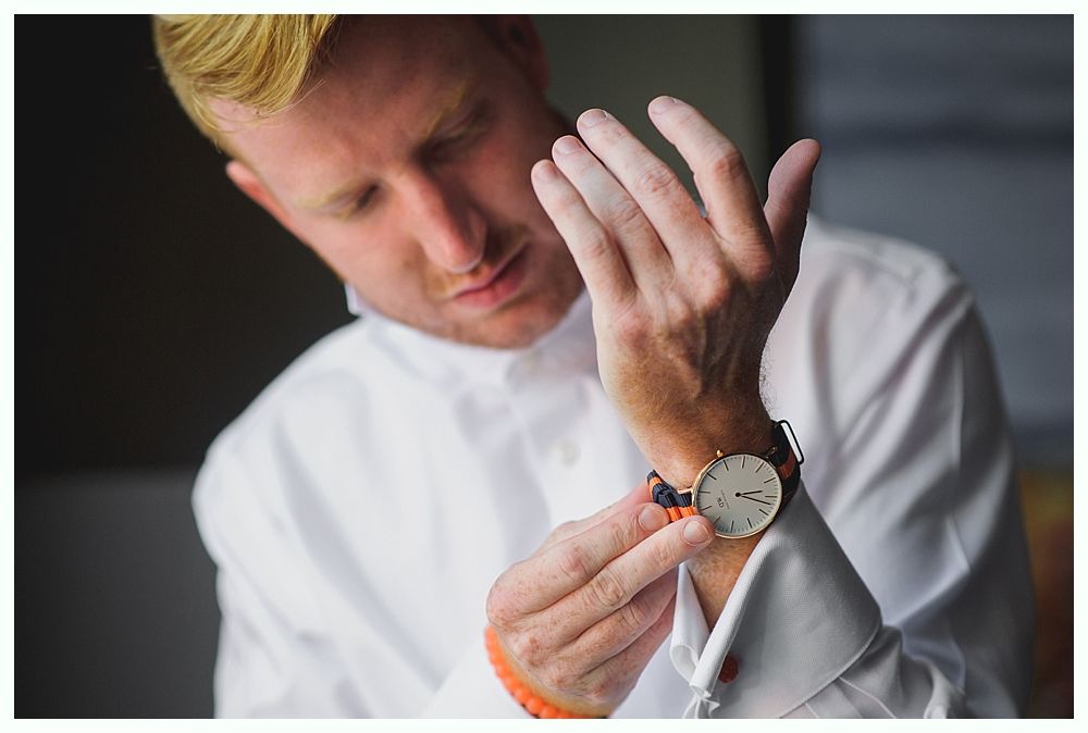 Man in white shirt adjusts a wristwatch, focusing on his wrist.
