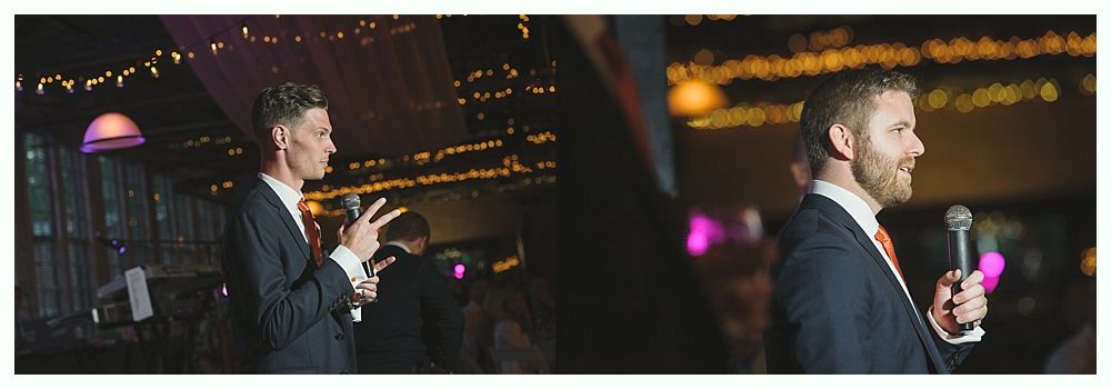 Two men in suits speaking into microphones, possibly at an event. Dark background with lights.