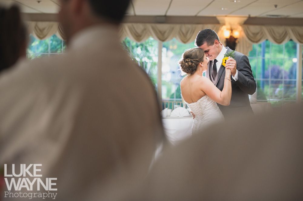 Bride and groom dancing, in a ballroom with draped windows. The groom wears a suit; the bride a strapless dress.
