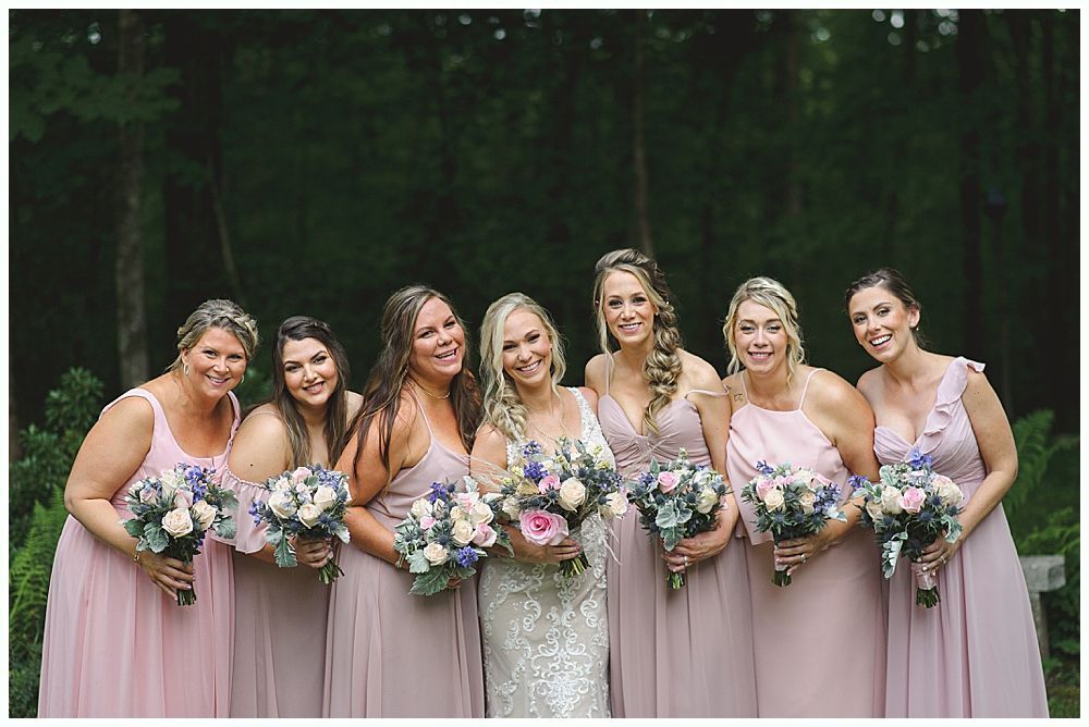 Bride smiles at the altar during a ceremony. Groomsmen in suits partially block view. Outdoor setting.