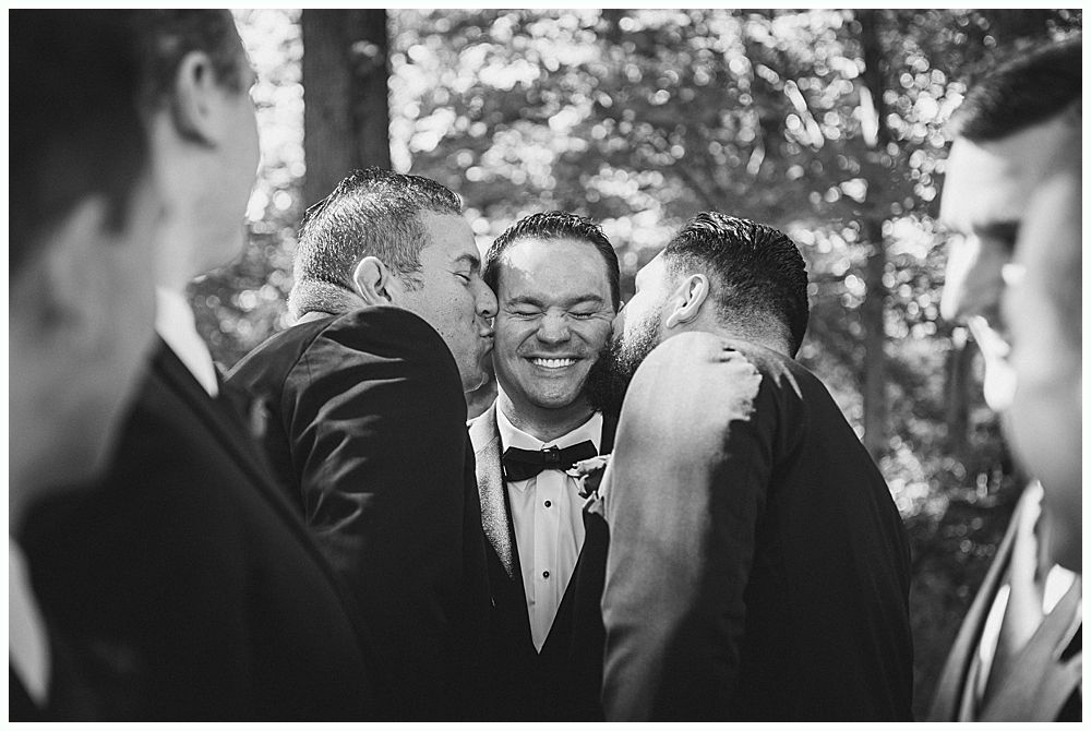 Wedding ceremony outdoors by a lake with a couple, wedding party, and guests under a cloudy sky.