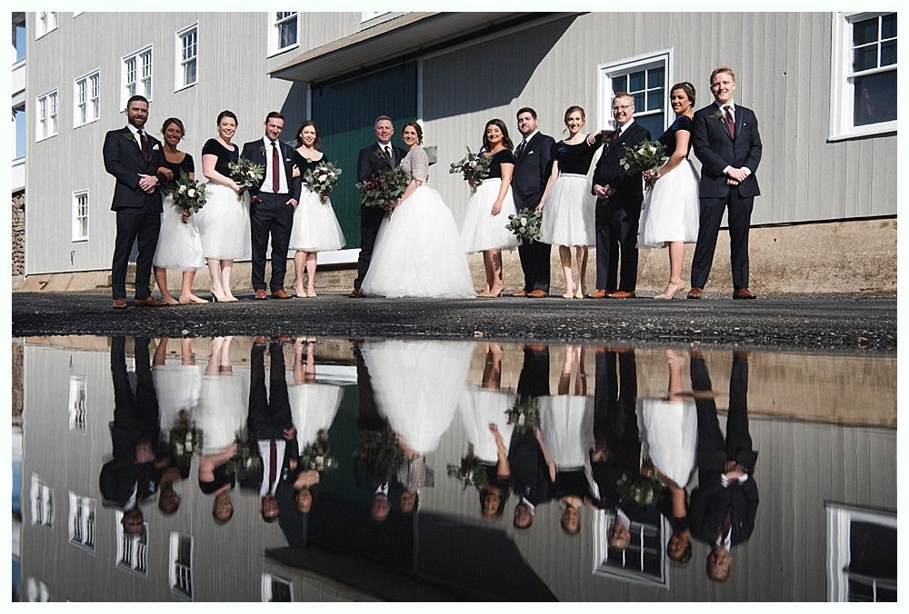 Newlyweds celebrating with champagne outside a building. Bride holding bouquet and bottle. Another person laughs in the background.