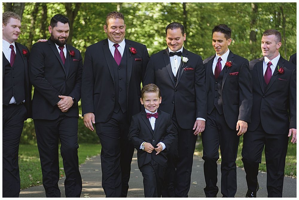 Newlyweds exiting outdoor wedding ceremony, holding hands, smiling. Wedding party applauds.