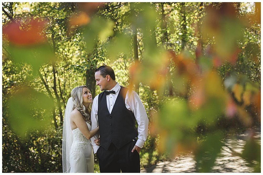 Bride in a white wedding dress smiles, looking over her shoulder as her veil blows in the wind outdoors.
