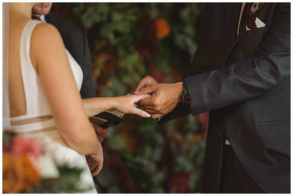 Couple in wedding attire embrace under a large weeping willow tree on a grassy hill.