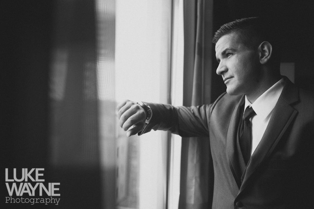 Man in suit looks out a window, checking his watch, waiting. Black and white.