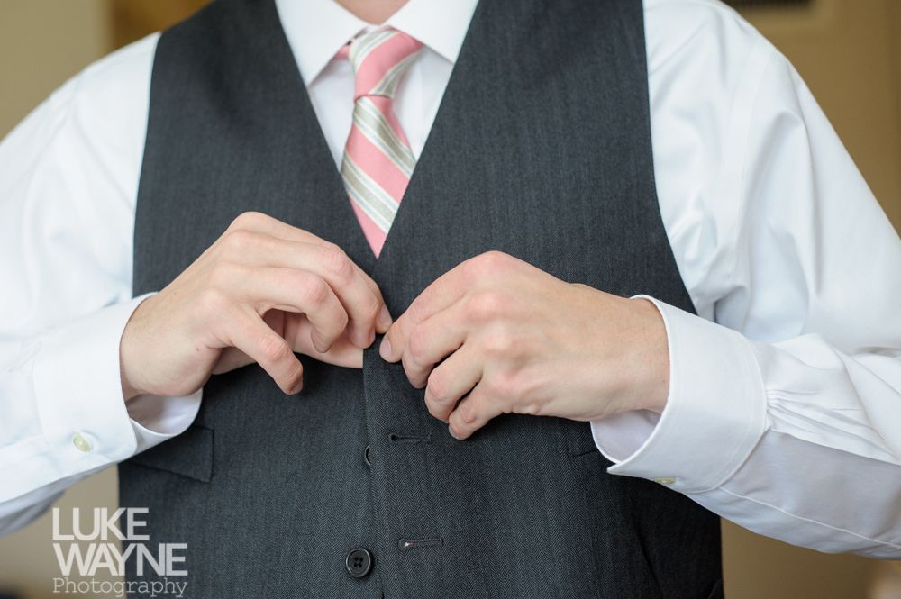 Man buttoning dark vest over white shirt and pink striped tie.