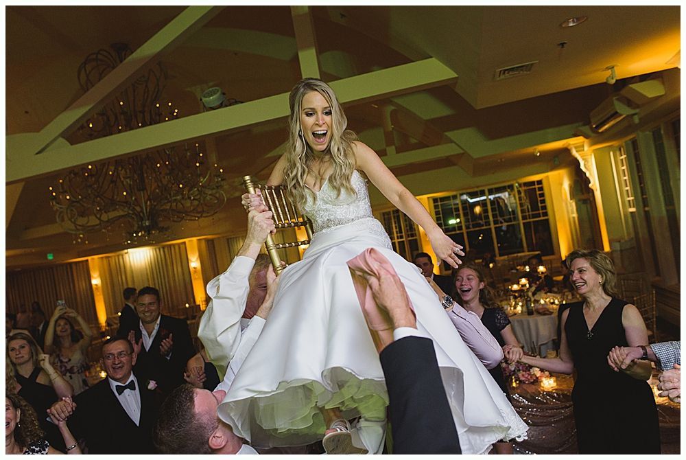 Bride and groom embrace outdoors, veil billowing, wedding bouquets visible.