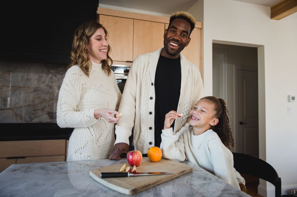 Family in kitchen smiling; cutting fruit on counter.