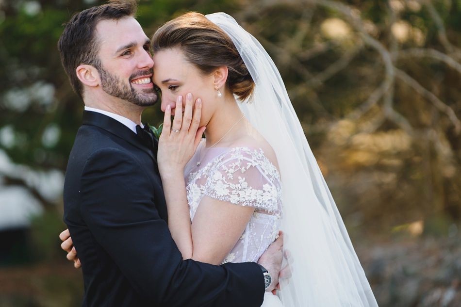 Bride with arms up, making a funny face, groom looking at his hand, cake cutting in background.