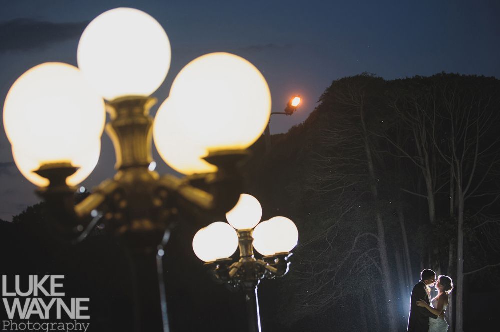 Couple embraces under a light at dusk; silhouetted against a mountain backdrop.