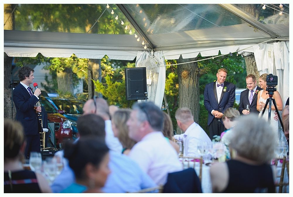 Bride with arms up, making a funny face, groom looking at his hand, cake cutting in background.
