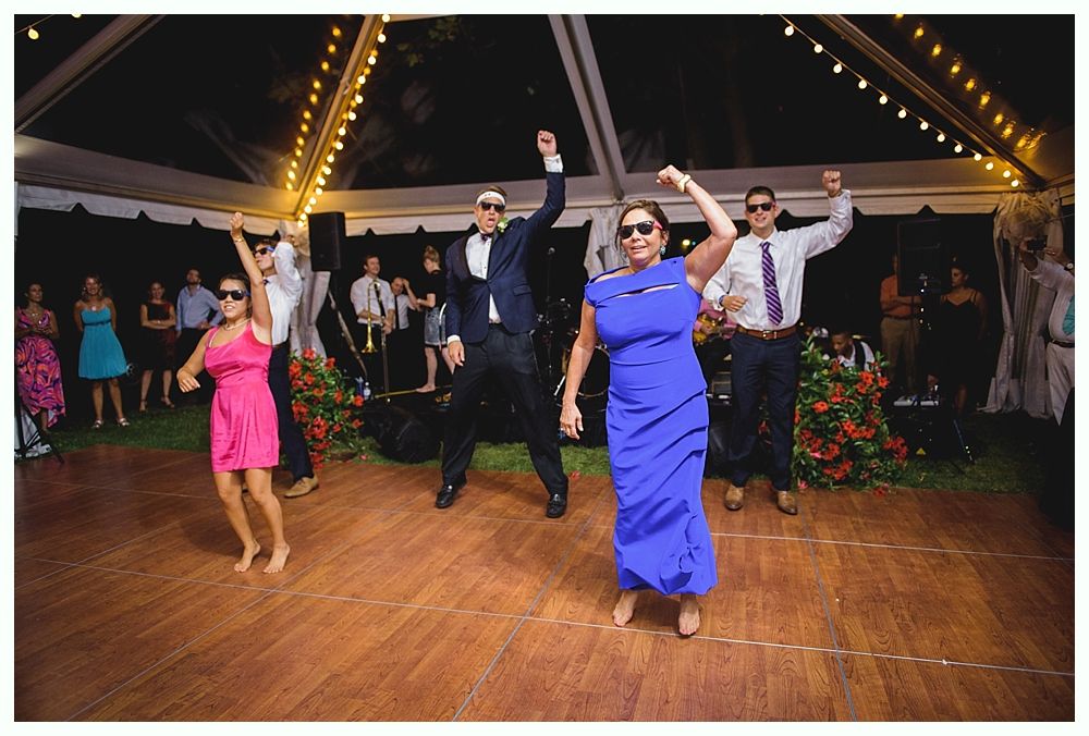 Bride with arms up, making a funny face, groom looking at his hand, cake cutting in background.