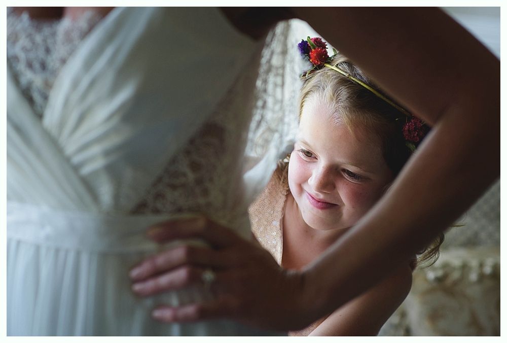 Bride with arms up, making a funny face, groom looking at his hand, cake cutting in background.