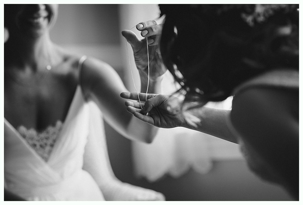 Bride with arms up, making a funny face, groom looking at his hand, cake cutting in background.