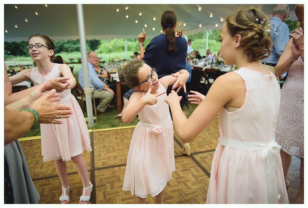 Bride with arms up, making a funny face, groom looking at his hand, cake cutting in background.