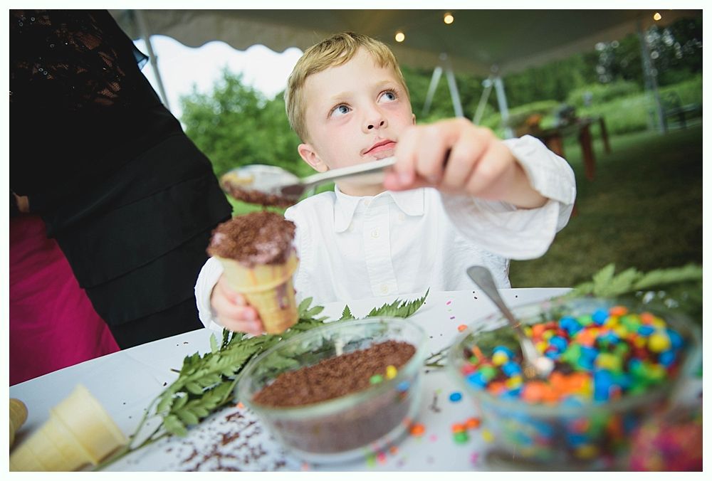 Bride with arms up, making a funny face, groom looking at his hand, cake cutting in background.