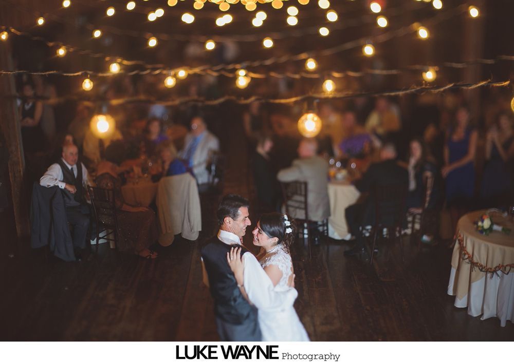 Wedding couple at night, poses near ivy-covered tower and building with string lights.
