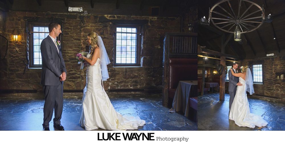 A bride and groom in a rustic venue, she is holding a bouquet, they embrace and dance together.