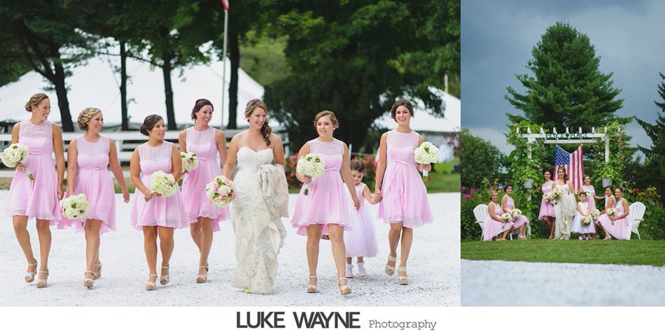Bride with bridesmaids in pink dresses walk on a gravel path. Wedding ceremony setting.