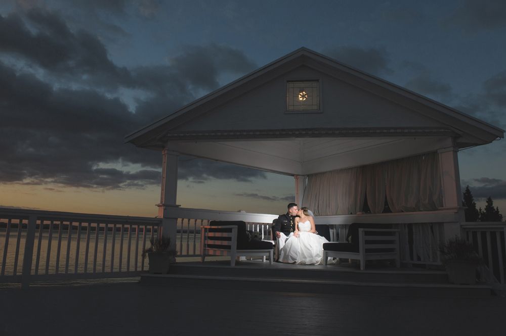 Bride and groom pose near dart boards. Bride in white dress, groom in suit. Indoor setting, red velvet ropes.